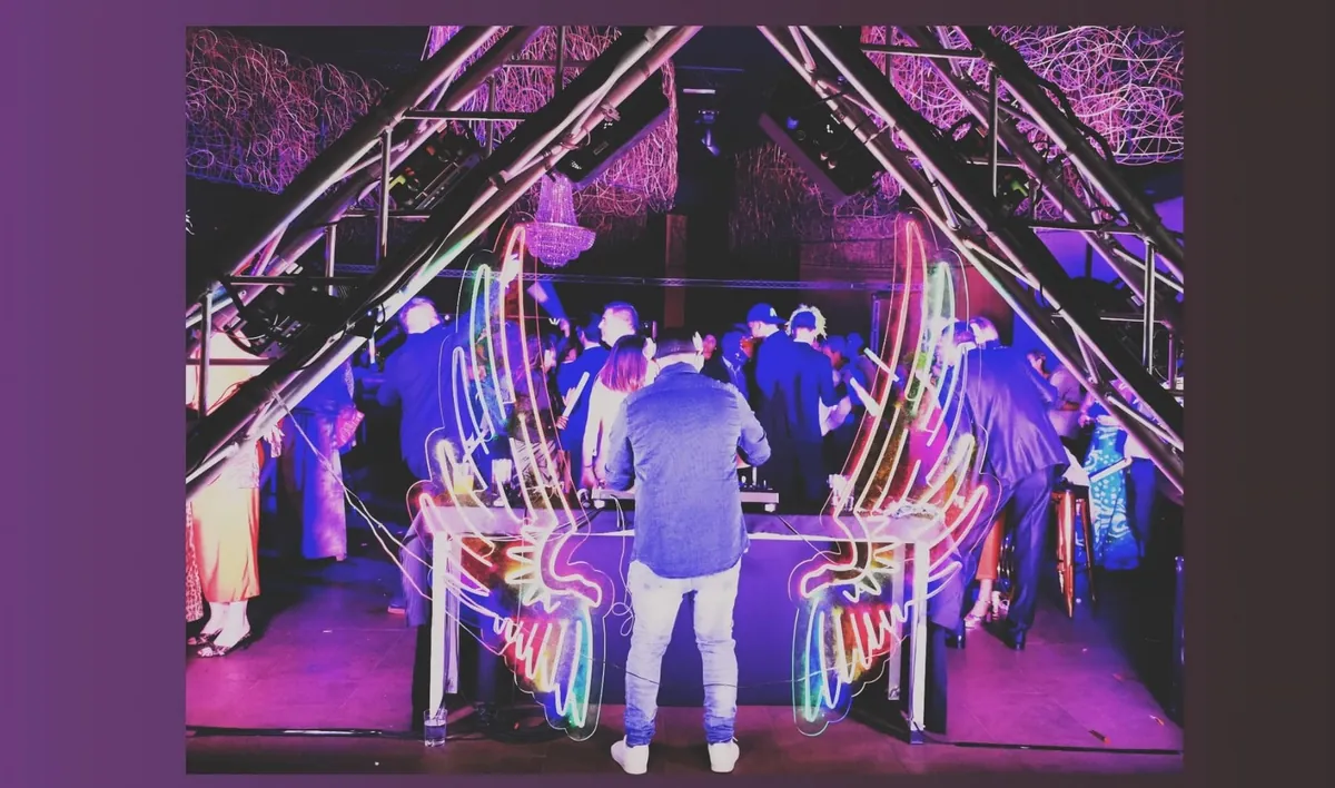 Cabina de DJ con luces de neón y público bailando en una fiesta